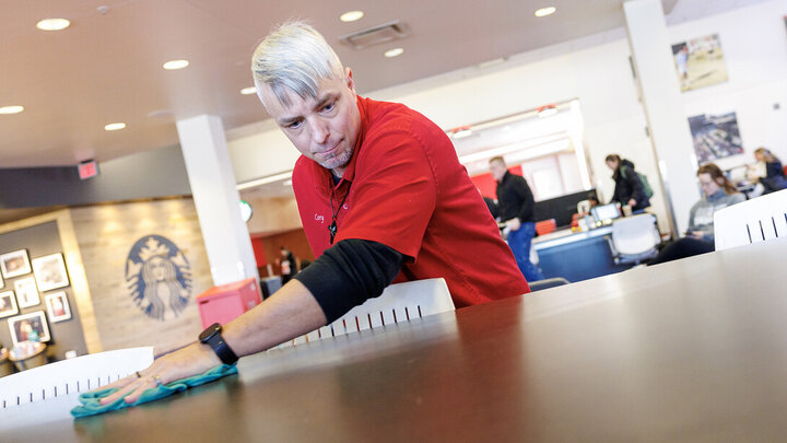 Cory Densberger, a hospitality service associate in the Nebraska Union, wipes a table clean in the food court. Densberger's outgoing personality has positive connections with students, faculty, staff and campus visitors. He's also been honored with three Parent's Association awards, which require nominations from students. [Jordan Opp | University Communication and Marketing]