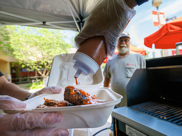 A cook adds Oklahoma BBQ sauce to an order of ribs at an East Campus grill out. [Craig Chandler | University Communication and Marketing]